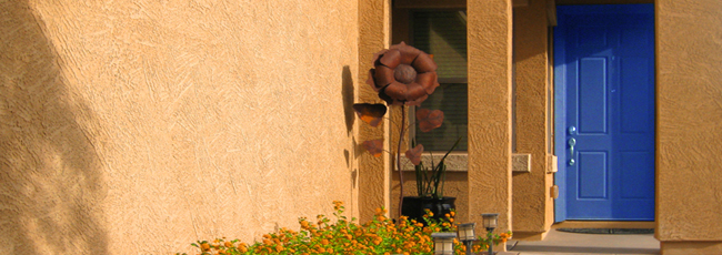 Sun shining on stucco home with bright blue door, walkway lined with yellow flowers and 6-foot metal sunflower sculpture - Welcoming front entrance - Bill Salvatore, Arizona Elite Properties 602-999-0952 - Arizona Real Estate