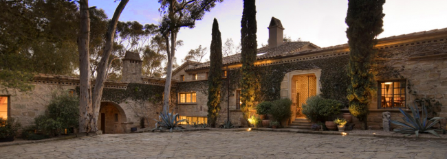 Stone exterior of villa style home at dusk with interior lights, massive stone driveway - Ellen DeGeneres and Portia de Rossi