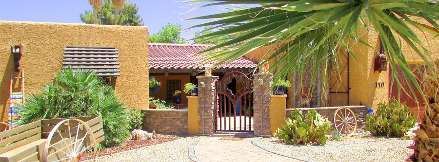 brick walkway through stone pillars and iron gate to courtyard with palm trees and flowering bushes - Front Landscaping - Bill Salvatore, Your Valley Property Team - Arizona Elite Properties 602-999-0952