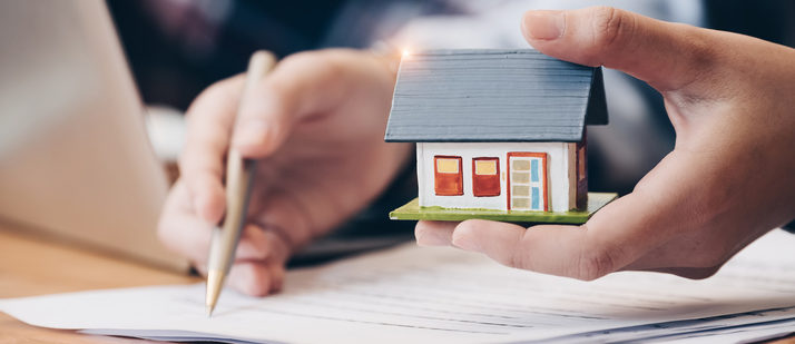 close up of hand holding small model house, while signing a contract - homeowners insurance, renovations and insurance, insurance for remodeling your home, property value - Bill Salvatore, Your Valley Property Team - Arizona Elite Properties 602-999-0952