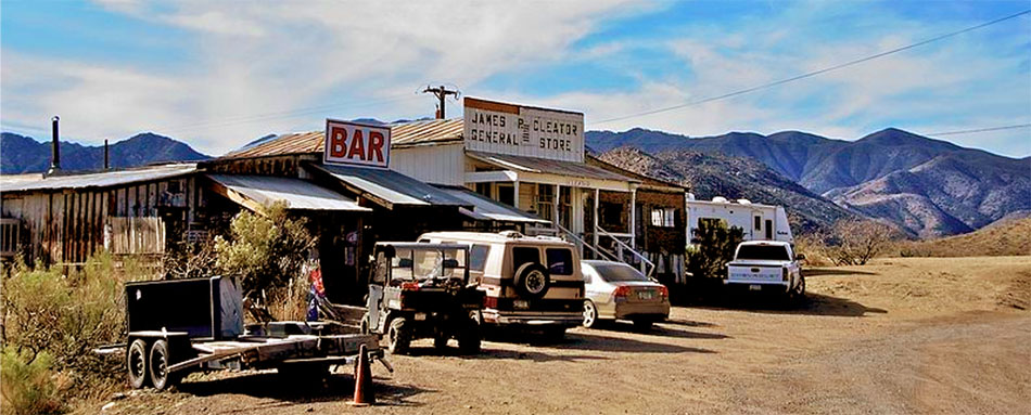 modern automobiles parked in front of a crumbling old town with bar and general store, with beautiful mountain range behind - Cleator AZ, Arizona Ghost Town for Sale - photo by Nic Lindh via Wikipedia - Bill Salvatore, Your Valley Property Team - Arizona Elite Properties 602-999-0952