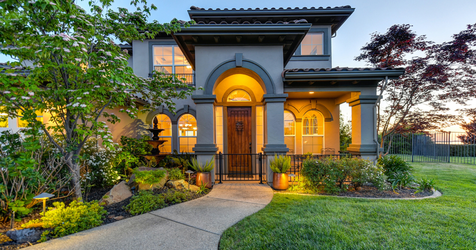 large gray home with columns and tile roof, lit at dusk, green lawn and walkway - Landscaping, front yard, curb appeal stephen-leonardi-via unsplash - Bill Salvatore, Your Valley Property Team, Arizona Elite Properties 602-999-0952