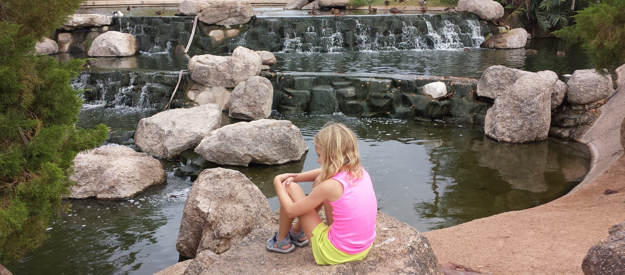 Girl sitting on rocks beside a waterfall - Freestone Park Gilbert AZ, Gilbert homes for sale, Best Places to Live - Bill Salvatore, Your Valley Property Team - Arizona Elite Properties 602-999-0952
