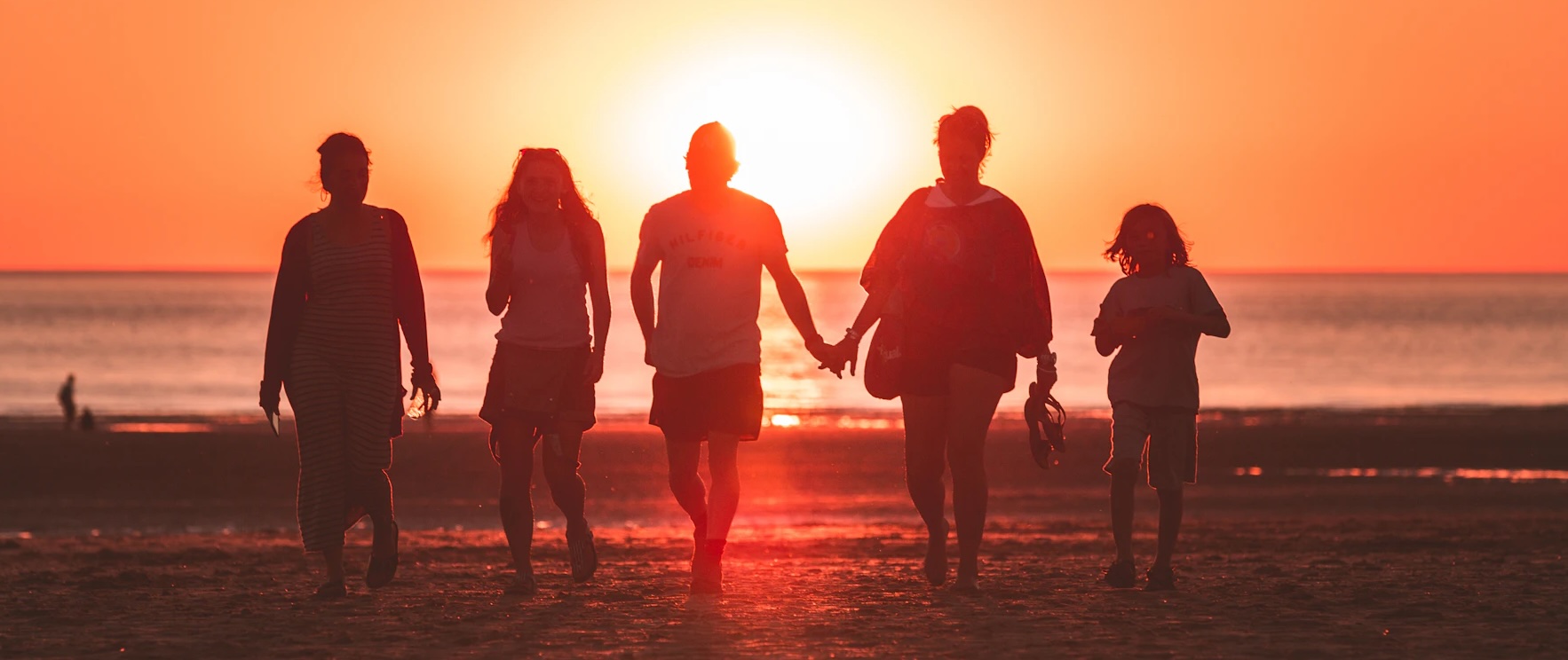 silhouettes of several people walking hand-in-hand in front of a sunset