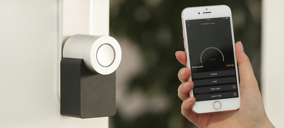 hand holding smartphone beside a digital thermostat on the wall